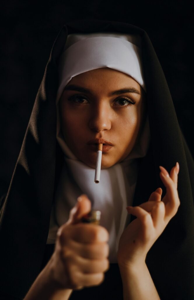 Portrait of a nun with a cigarette in mouth, holding a lighter against dark background.
